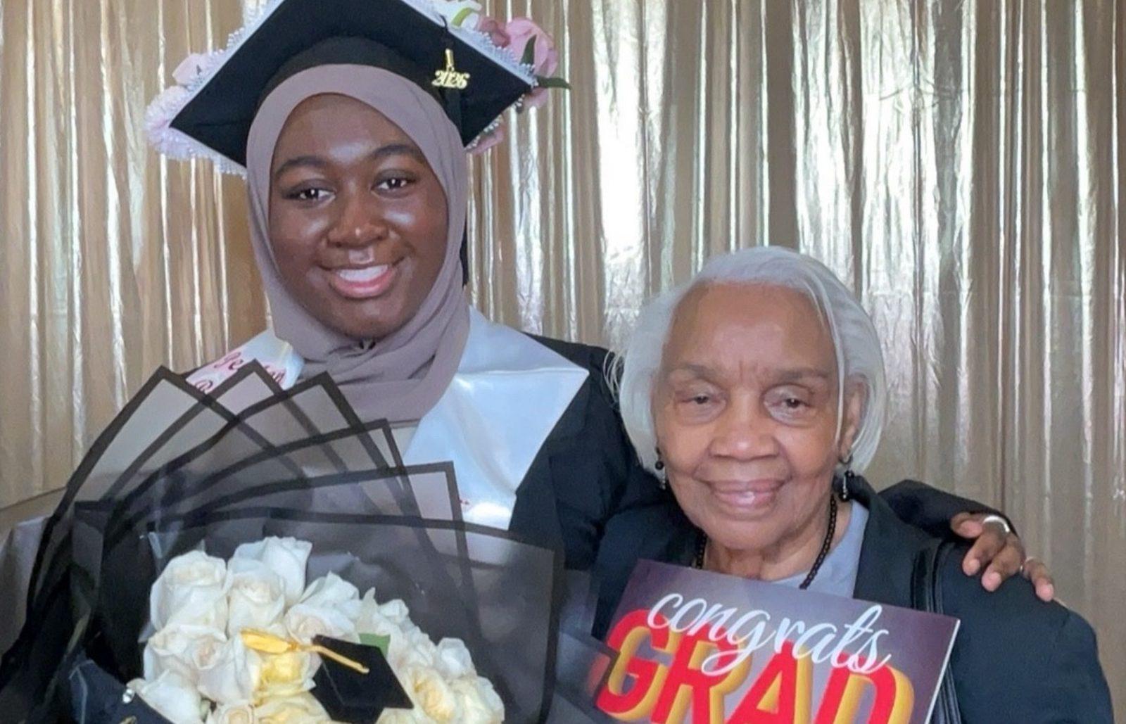 Graduate holding white roses beside her grandmother with a congrats grad sign in a photo booth