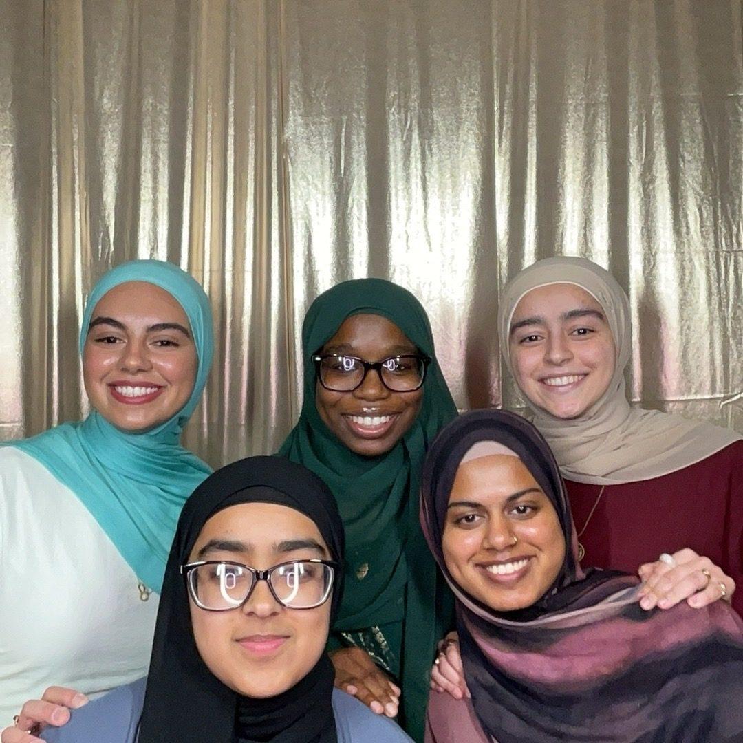 Five friends smiling in front of a shimmering gold photo booth backdrop