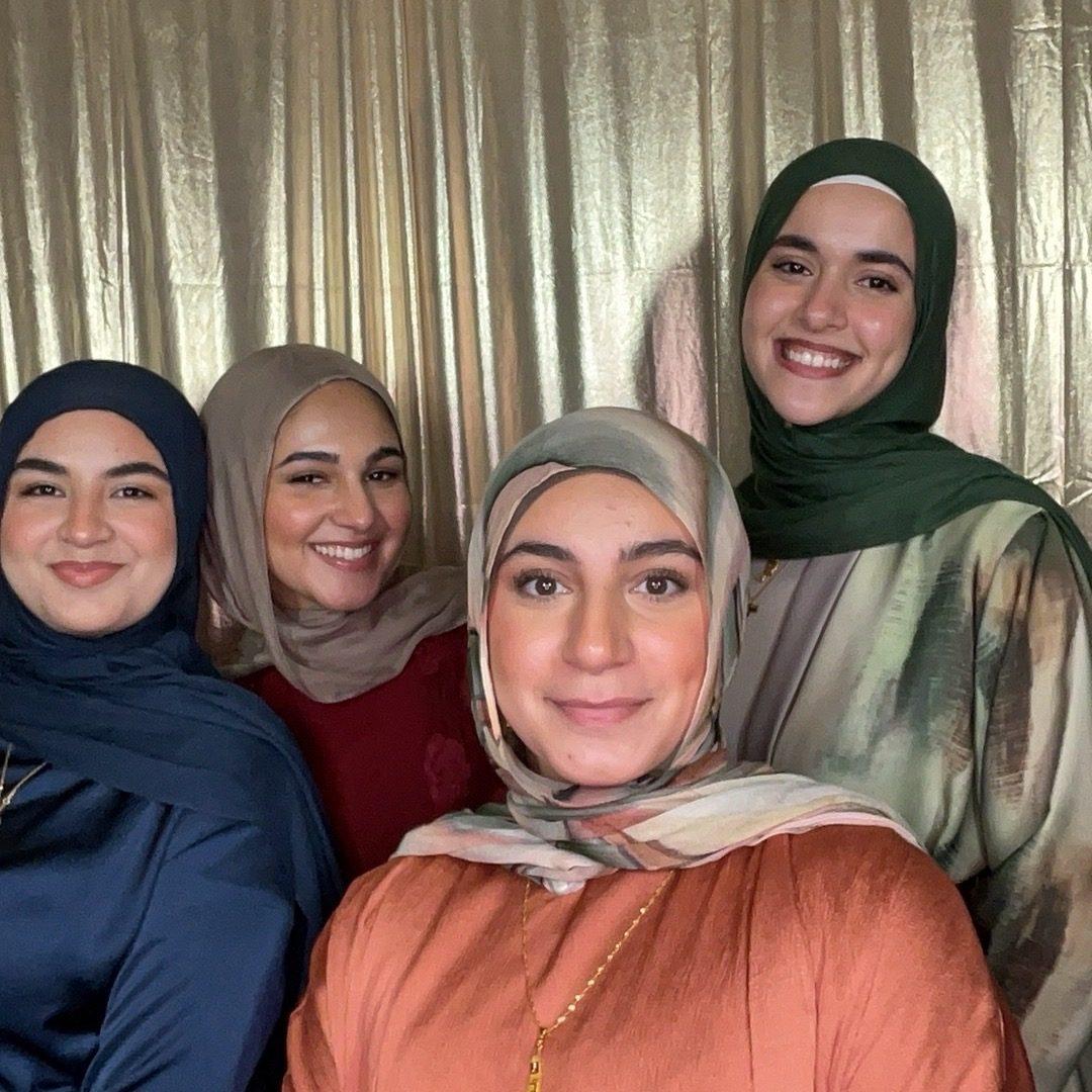Four friends smiling in a photo booth with a gold sequin backdrop at a university banquet